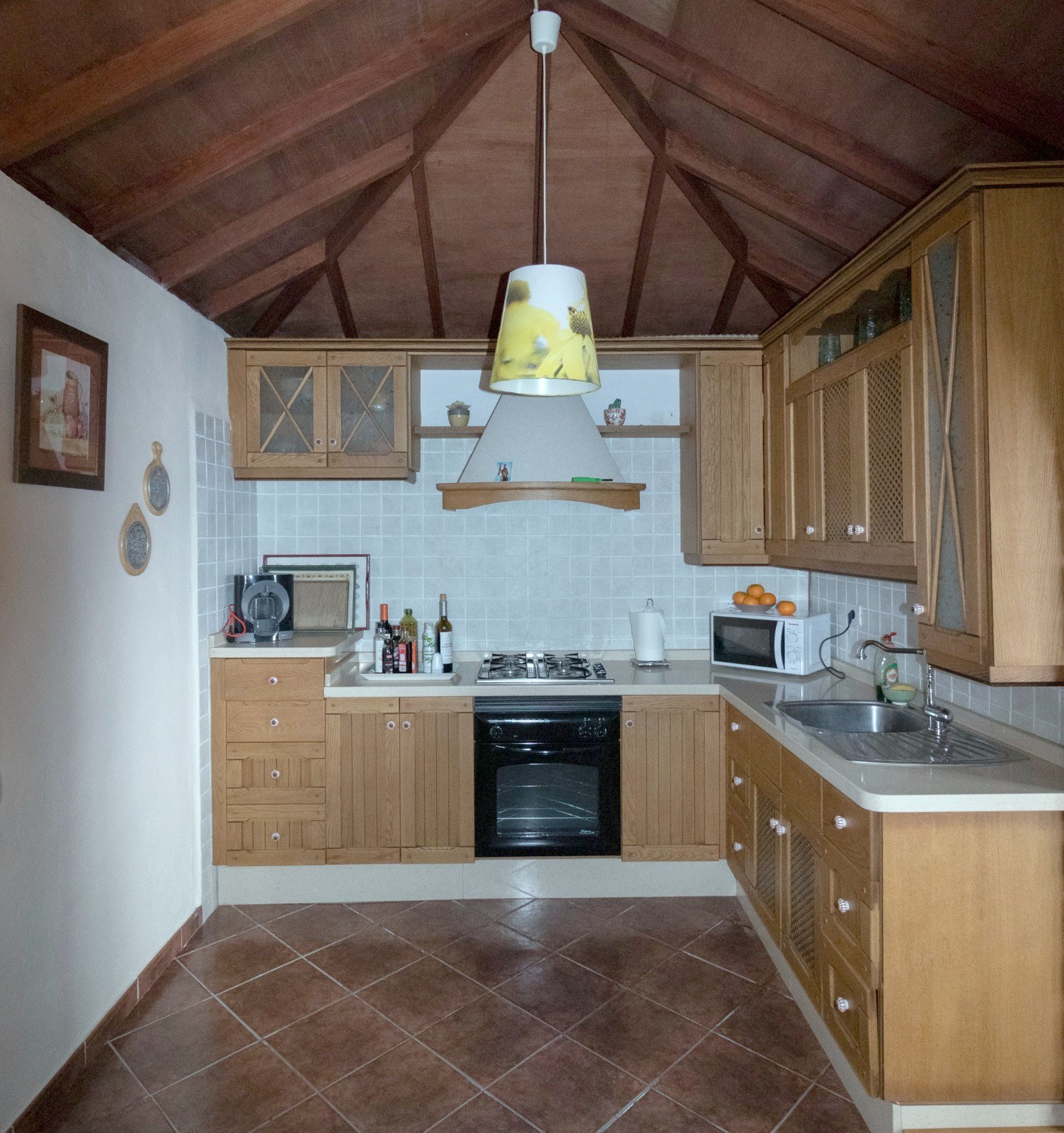 Cocina de Finca Julia con muebles de madera, techo de vigas a dos aguas, horno, placa de gas y microondas
