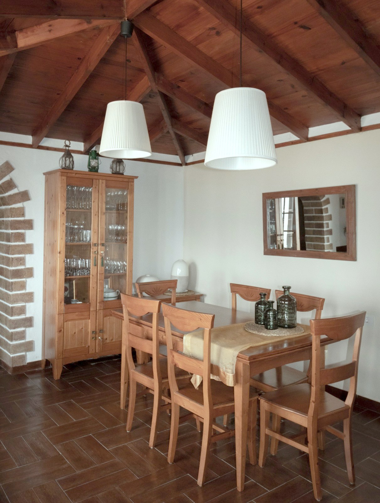 Comedor de Finca Julia con mesa y seis sillas de madera, vitrina con cristalería y techo de vigas vistas
