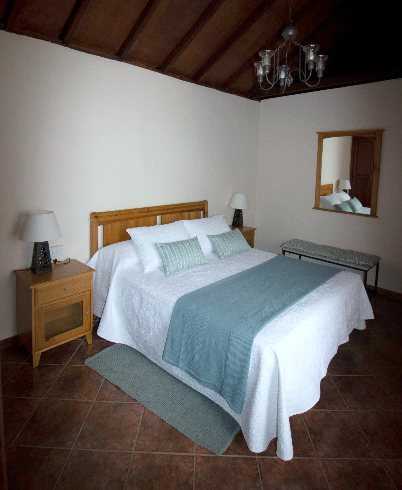 Dormitorio principal de Finca Julia con cama de matrimonio, mesillas de madera, banqueta y techo de vigas oscuras