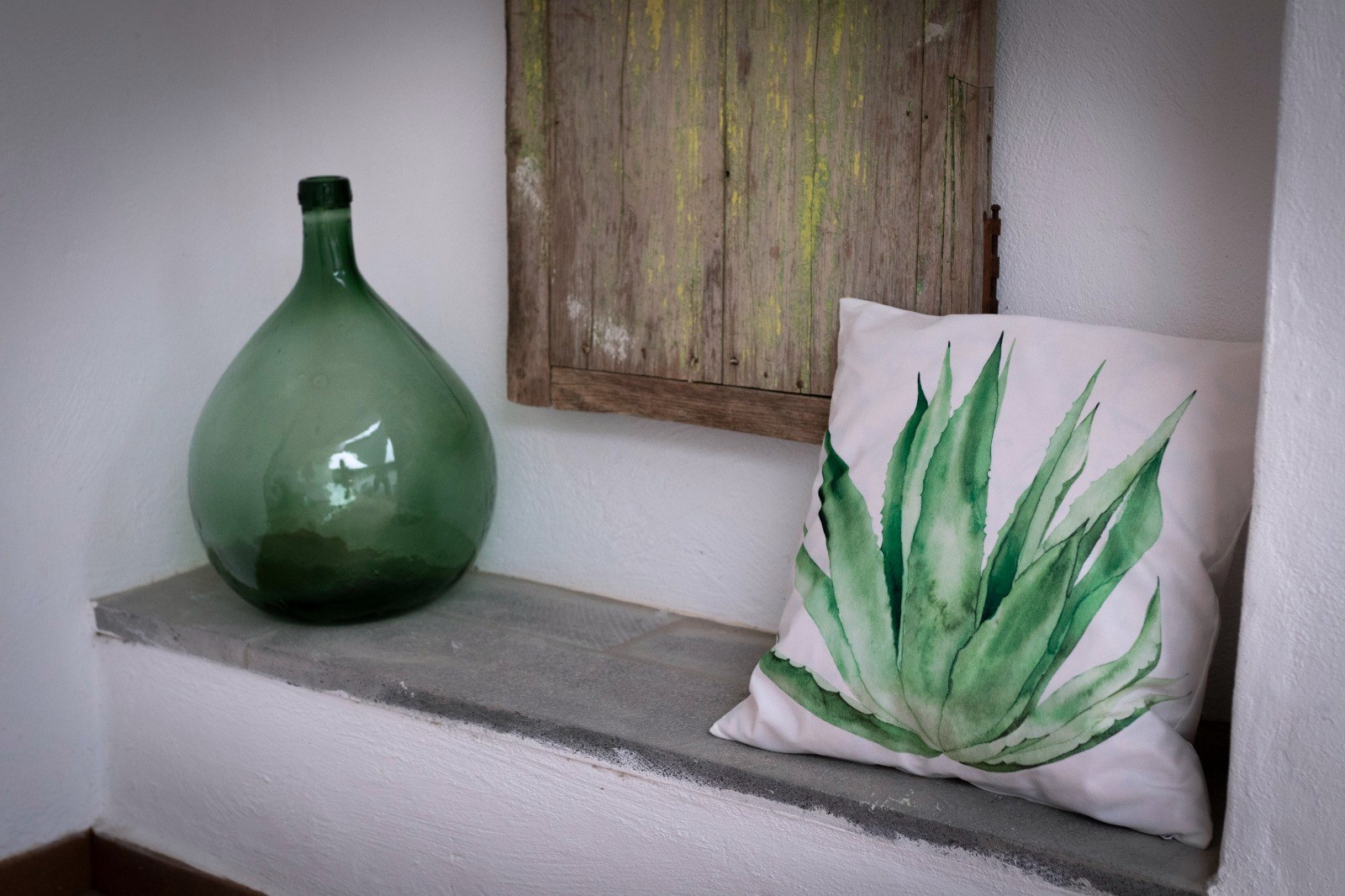 Damajuana de vidrio verde y cojín con una pitera pintada en una hornacina encalada de Finca Julia