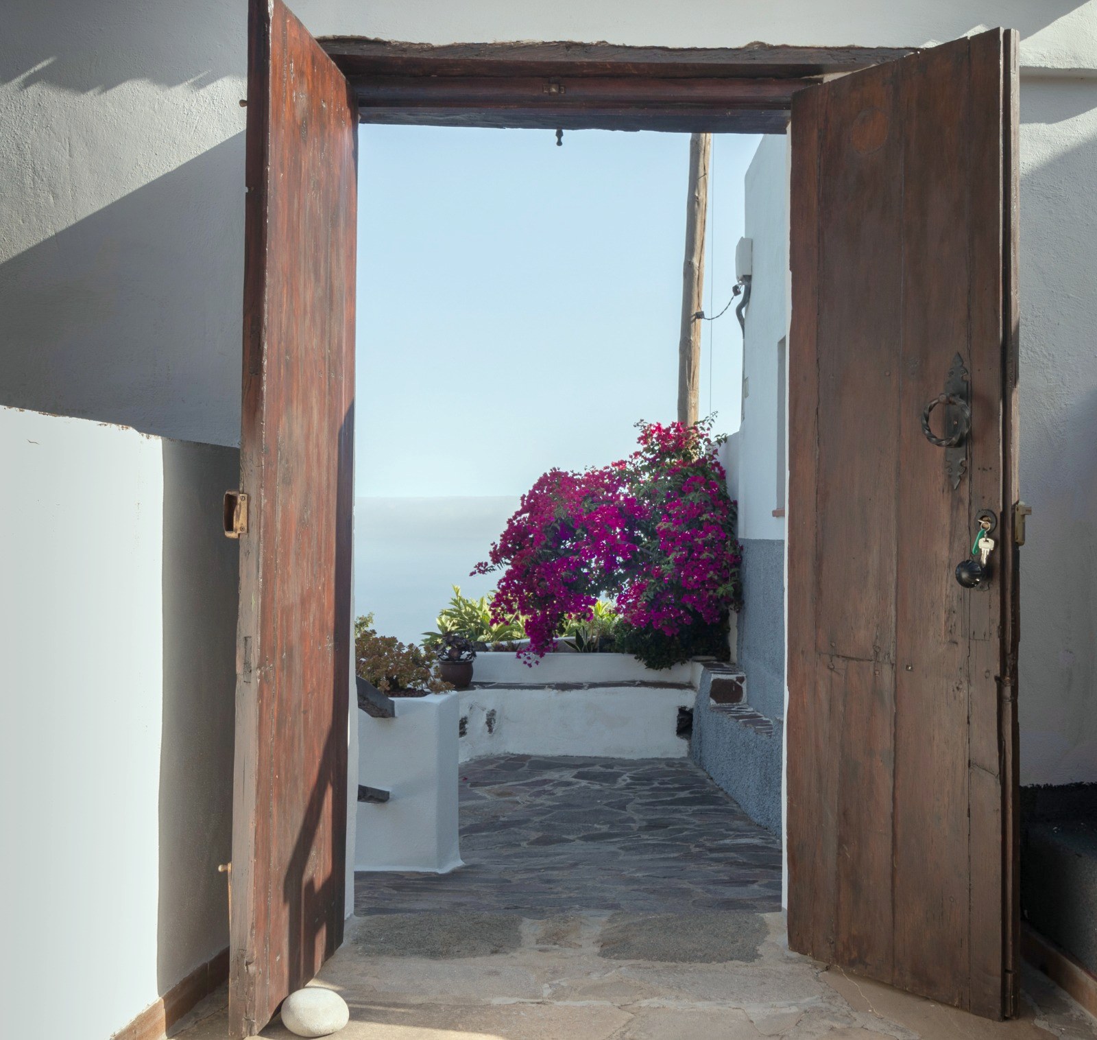 Puerta de madera antigua abierta desde el zaguán de Finca Julia a un patio encalado con buganvilla y el Atlántico al fondo