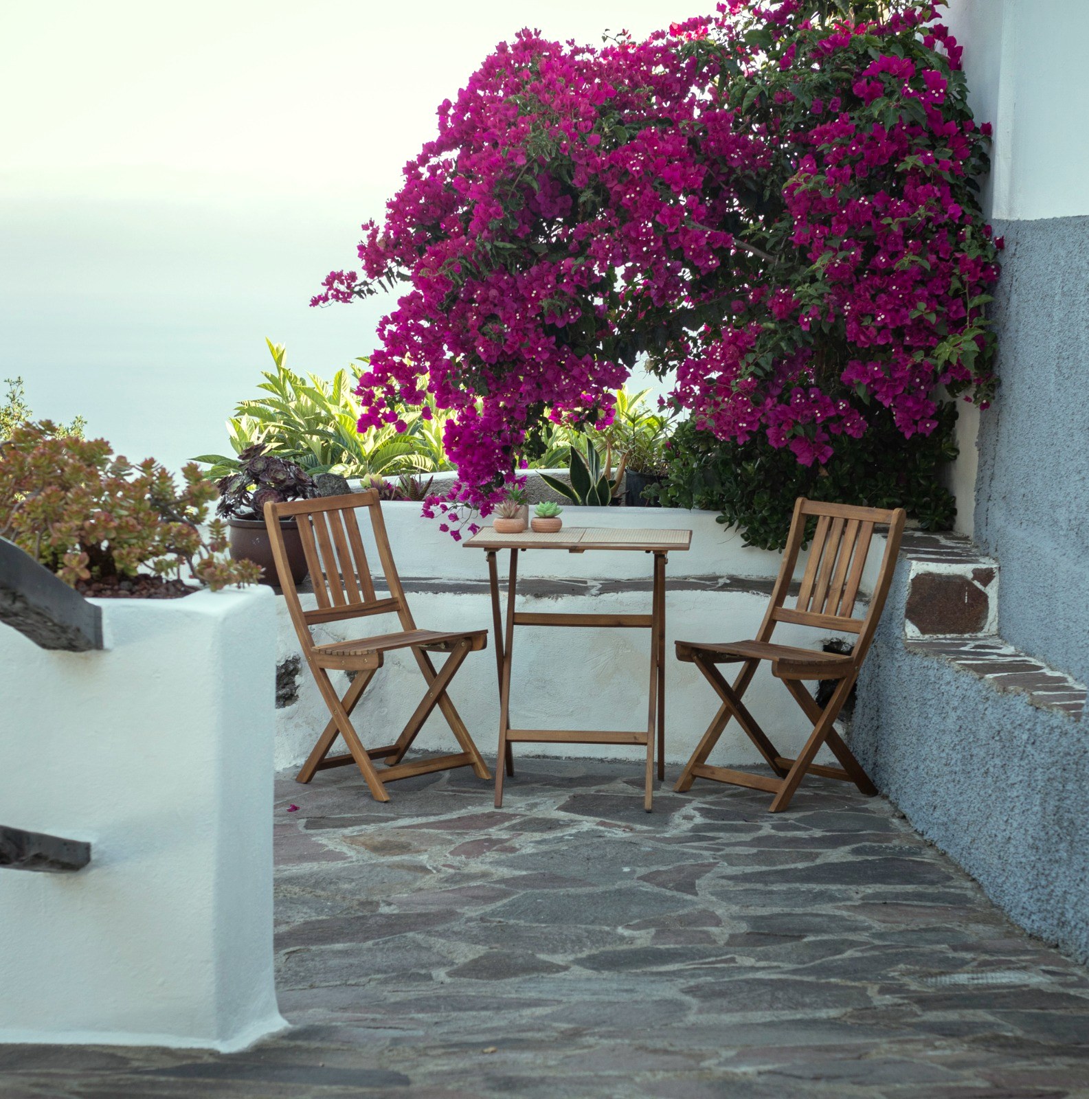 Terraza de Finca Julia con mesa y sillas plegables de madera, buganvilla en flor y el Atlántico de fondo